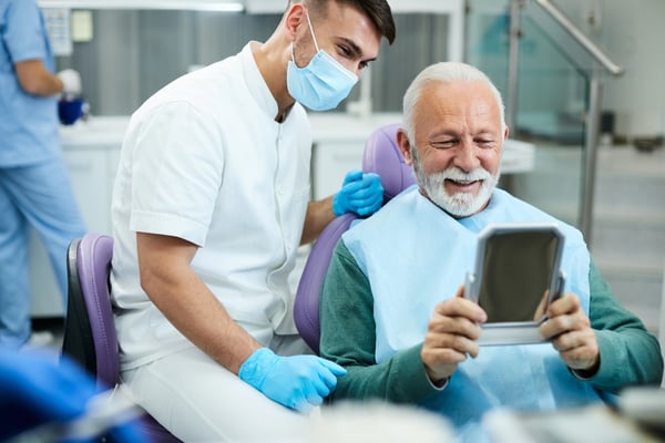 older male patient smiles in mirror as dentist looks on428089988