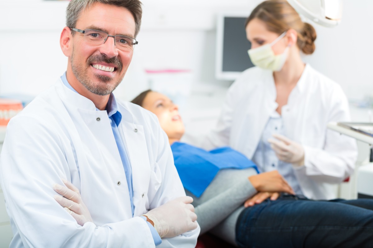 Smiling dentist while patient is helped by hygienist 56354003