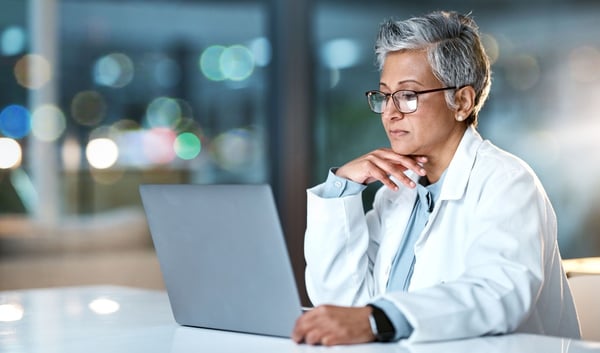 woman in a lab coat sits in front of laptop computer reading email 566596393
