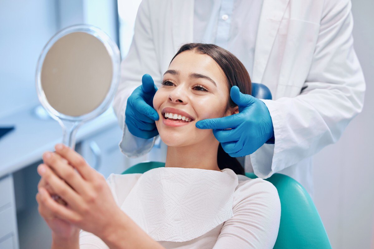 Dentist stands behind patient who smiles into a handheld mirror 606463645