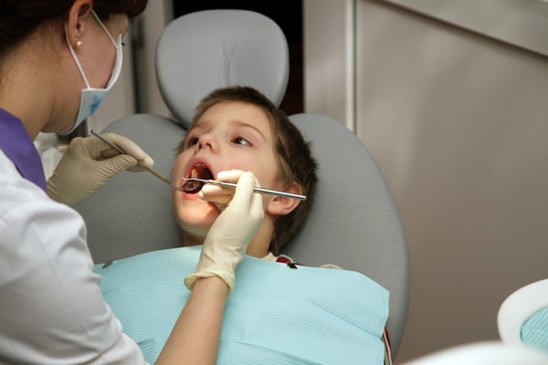 Patient in chair with mouth open while dentist checks teeth 6871897
